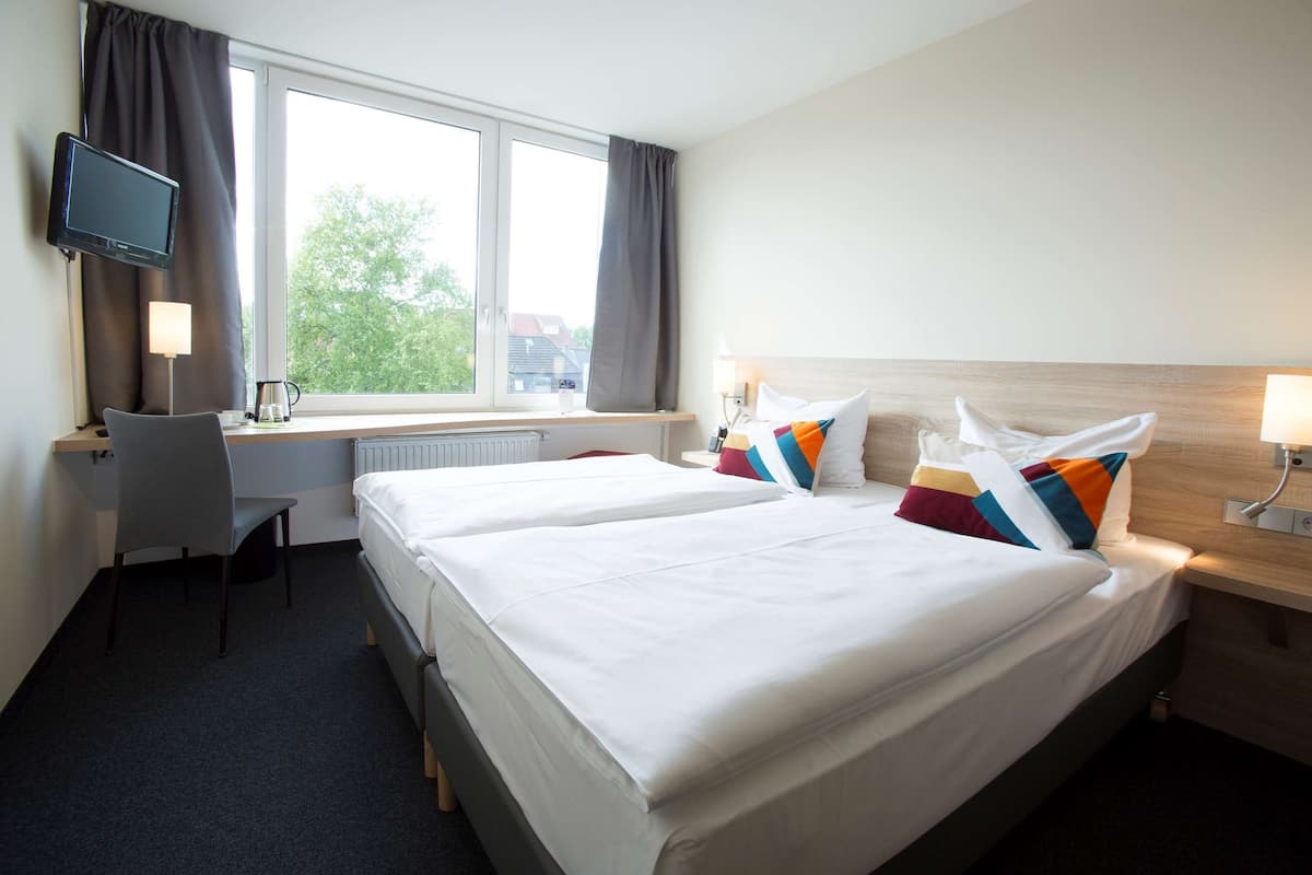 A hotel room with two beds, a desk, a chair, a TV, and a window with curtains.