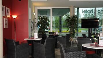 A restaurant with wicker furniture, indoor plants, and a TV screen.