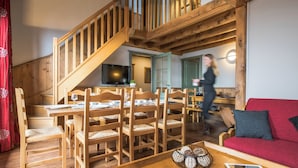 A wooden interior with a dining area, a staircase, a red sofa, and a television. - Résidences Village Montana by Les Etincelles  (Tignes)