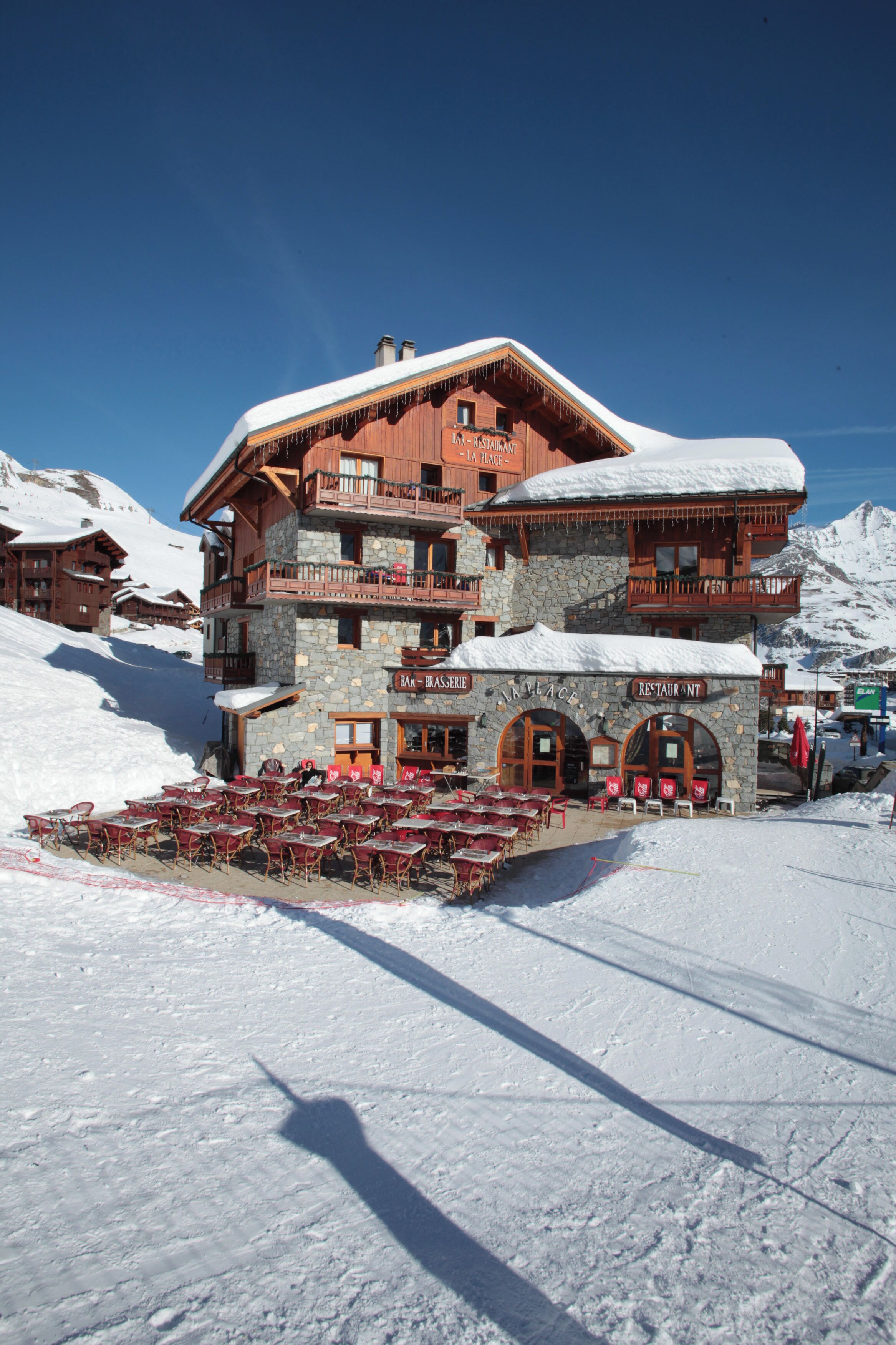 Un edificio de varios pisos con fachada de piedra y balcones de madera, rodeado de terreno cubierto de nieve.