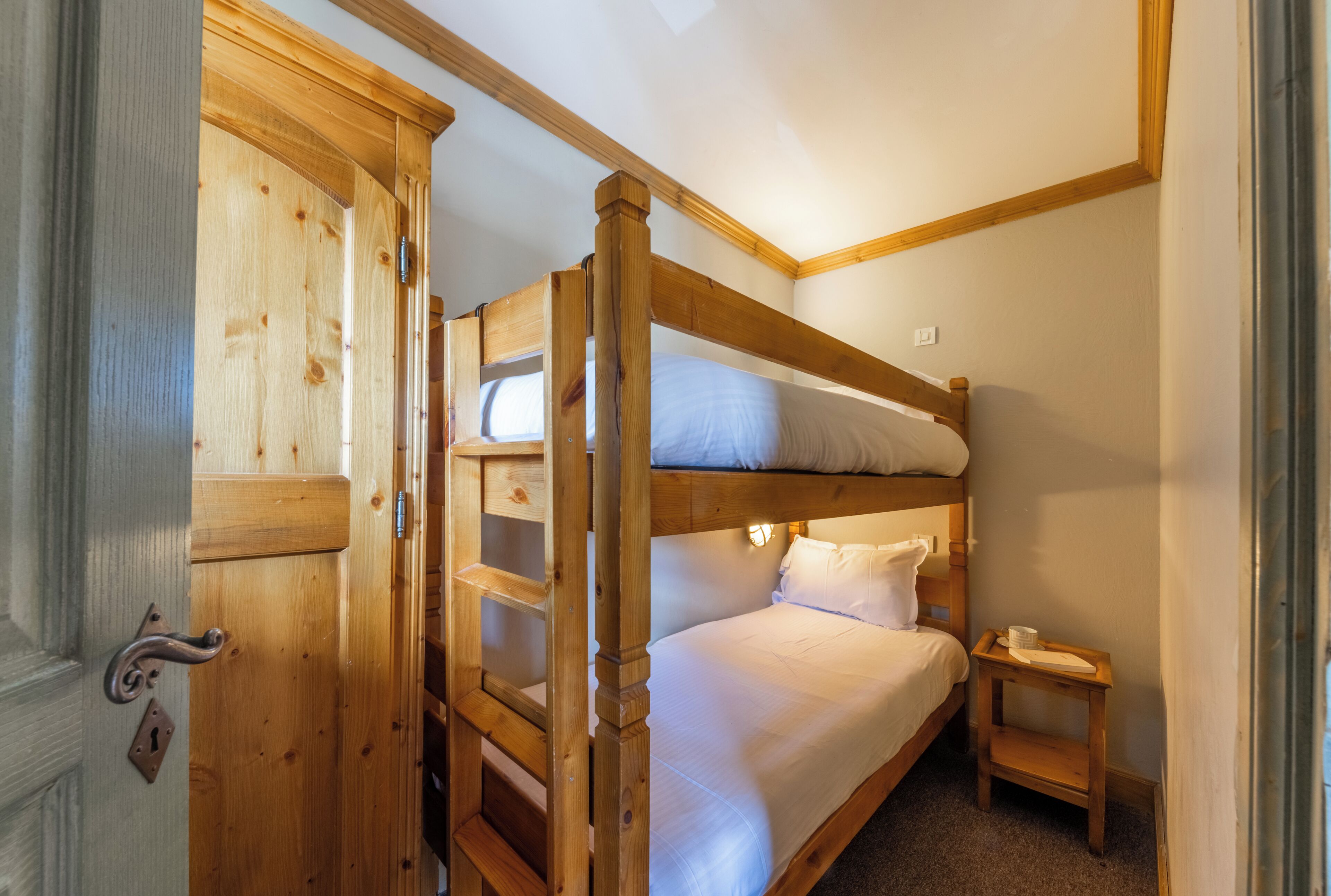 A bunk bed room with a wooden door and a small bedside table.