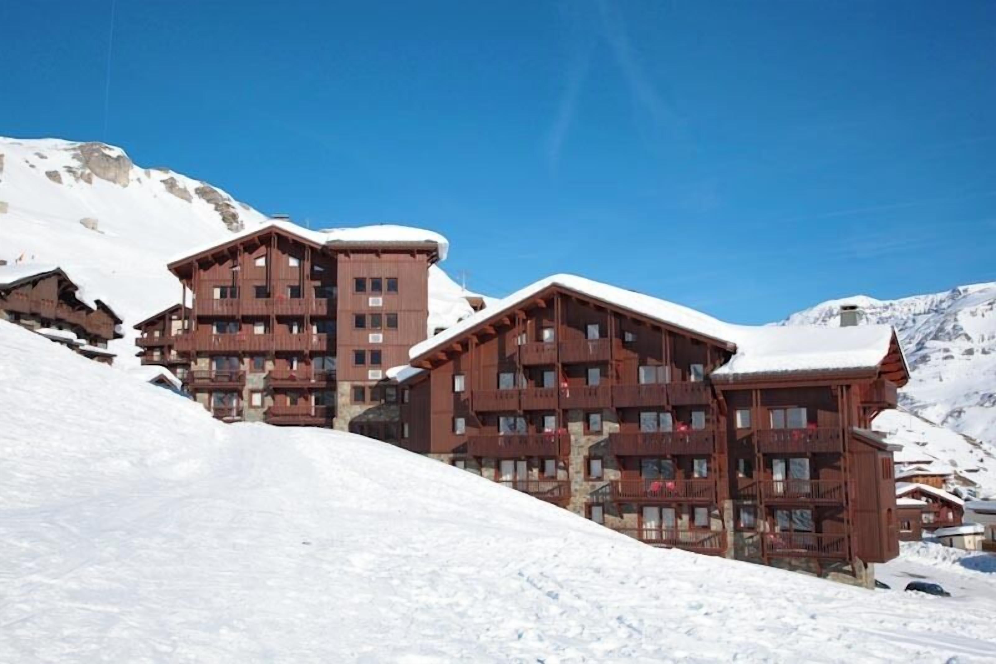 A multi-story wooden lodge with balconies, set against a snowy mountain backdrop.