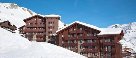 A multi-story wooden lodge with balconies, set against a snowy mountain backdrop.