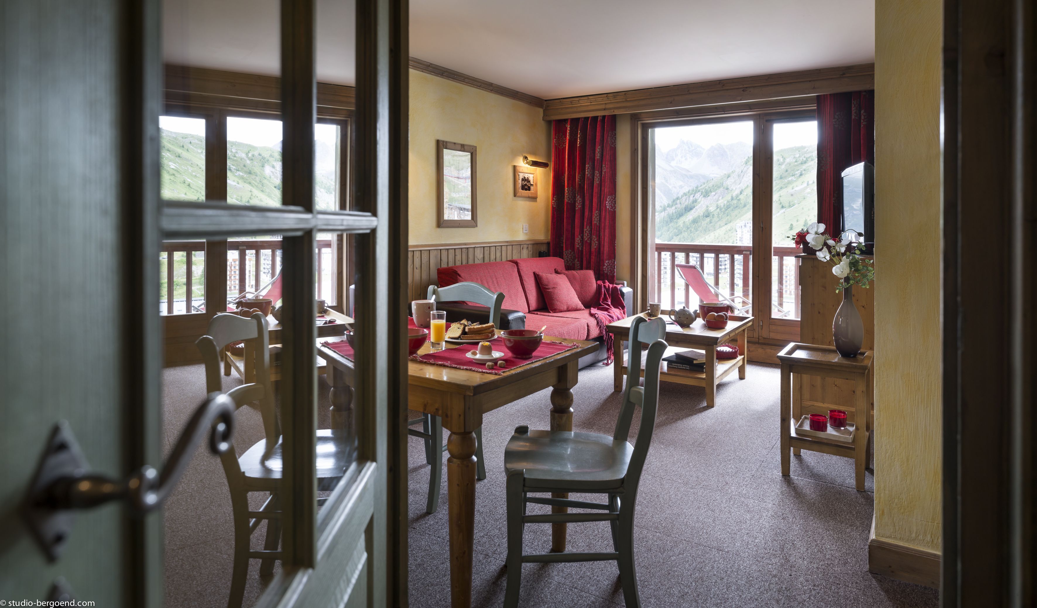 Una habitación acogedora con una mesa de madera, sillas, un sofá rojo y una ventana con vistas a la montaña.