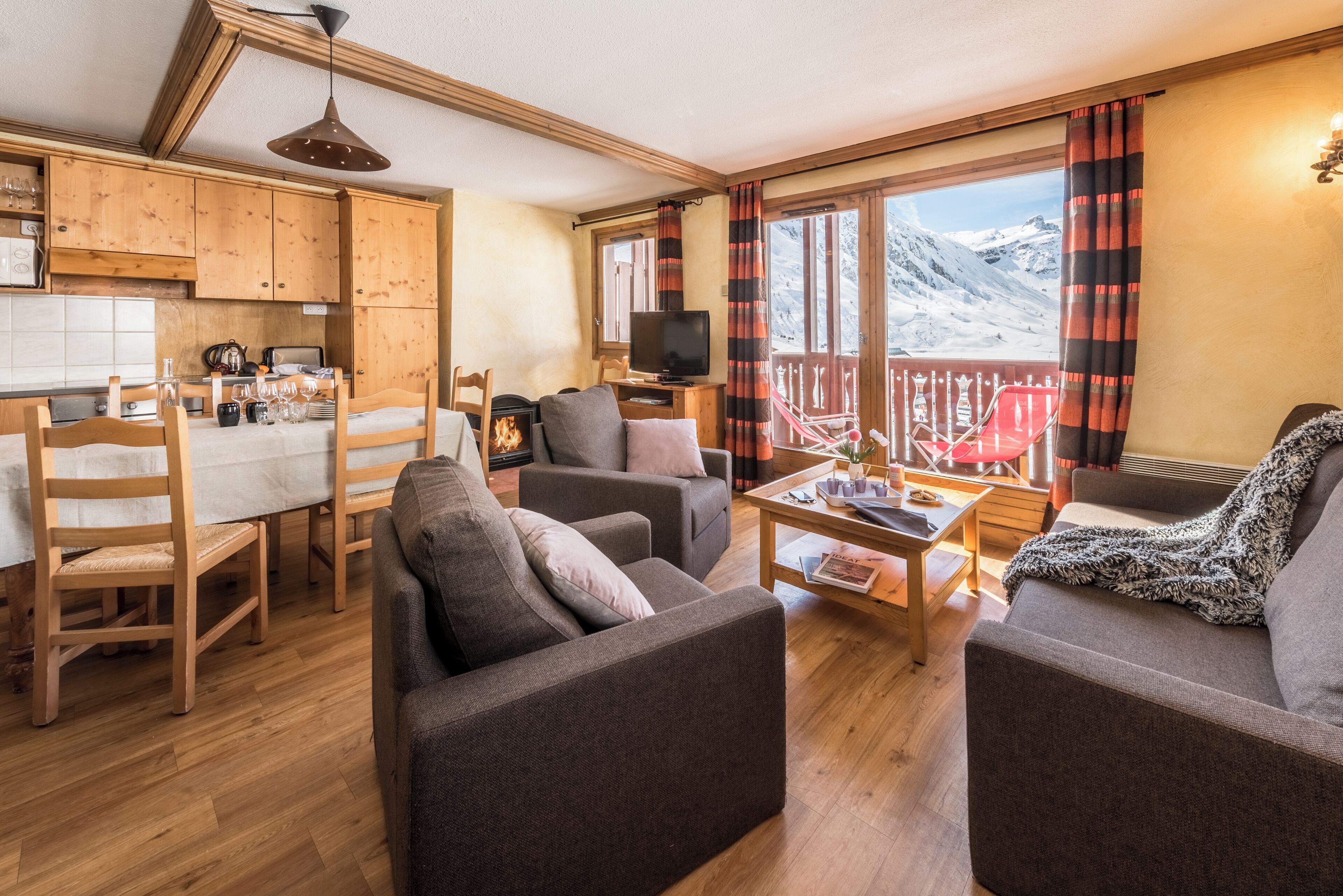 A cozy living room with a fireplace, wooden furniture, and a balcony with a mountain view.