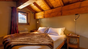 A wooden ceiling, a bed with white linens, a window with a view, and a nightstand with a cup. - Résidences Village Montana by Les Etincelles  (Tignes)