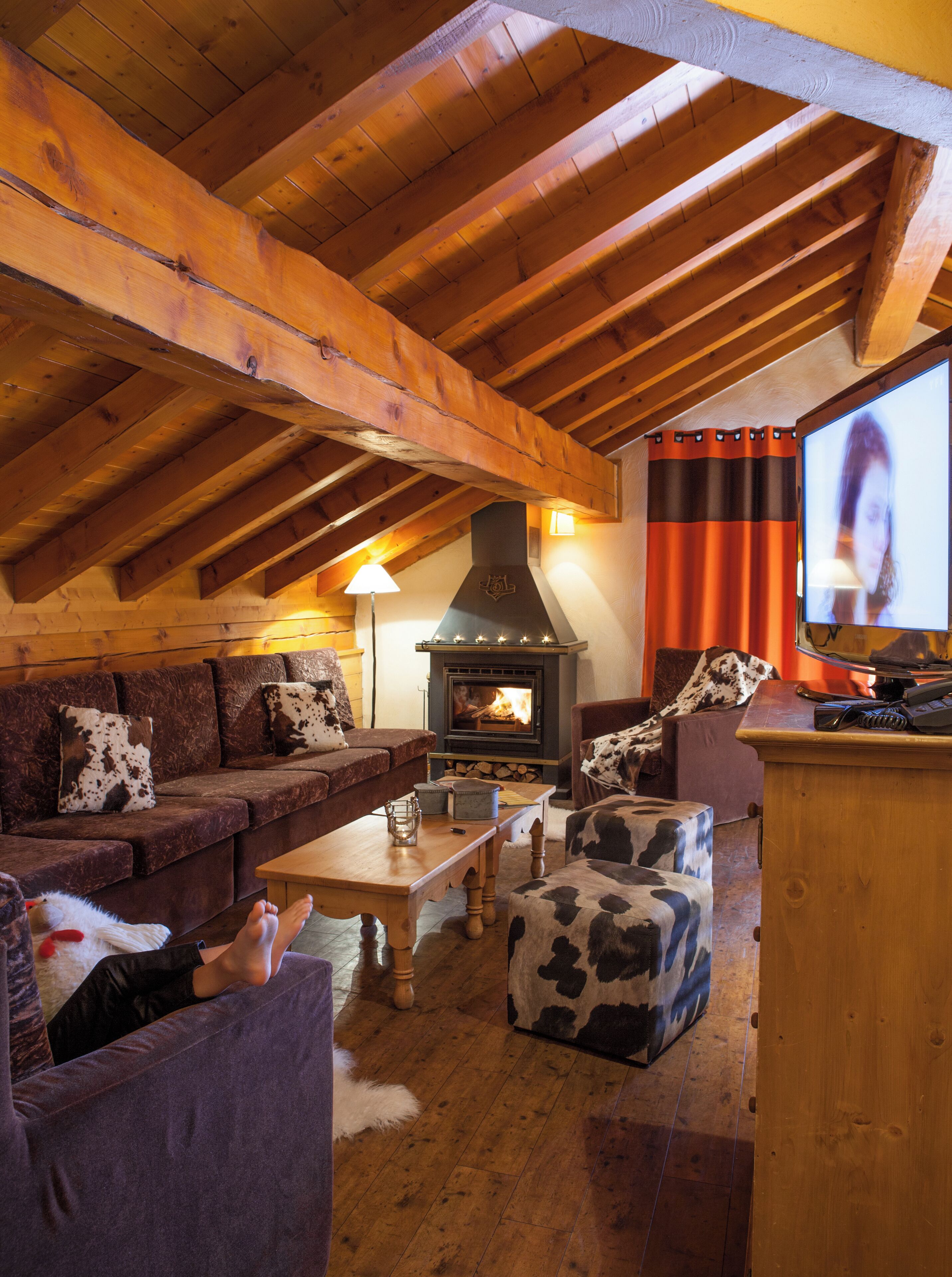 A cozy living room with a wooden ceiling, a fireplace, a television, and a couch with cowhide cushions.