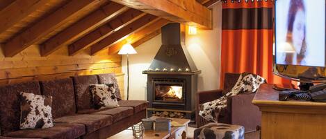 A cozy living room with a wooden ceiling, a fireplace, a television, and a couch with cowhide cushions.