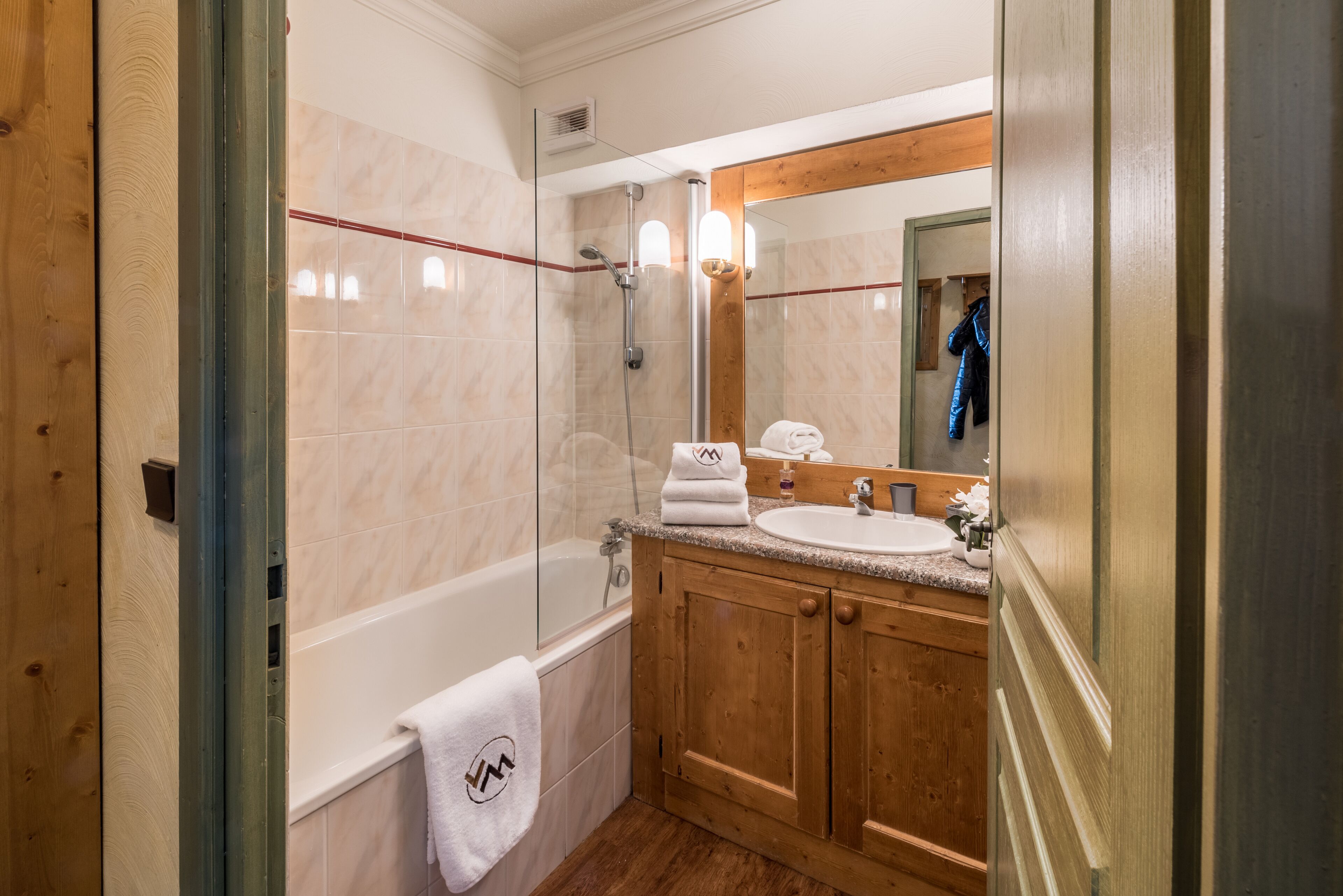 A bathroom with a glass-enclosed shower, a white bathtub, wooden cabinets, and a large mirror.