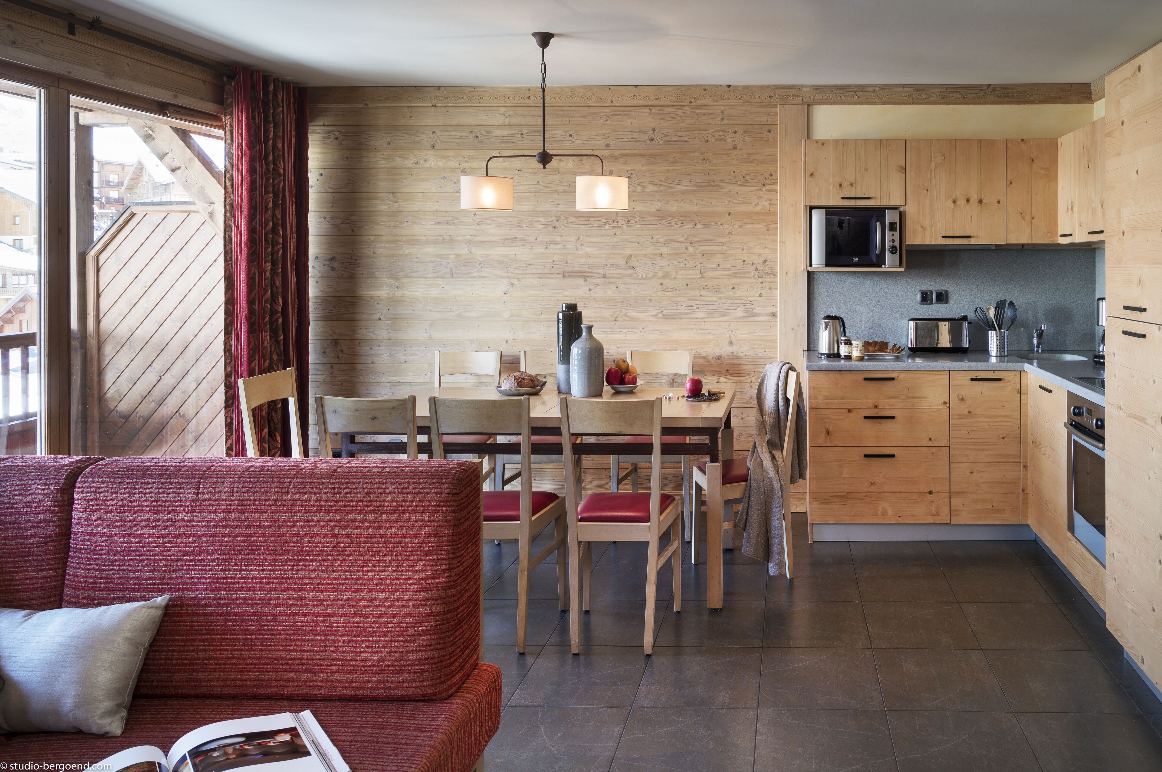 Une cuisine moderne avec des meubles en bois, un coin repas avec des chaises et un canapé rouge dans l’espace de vie.