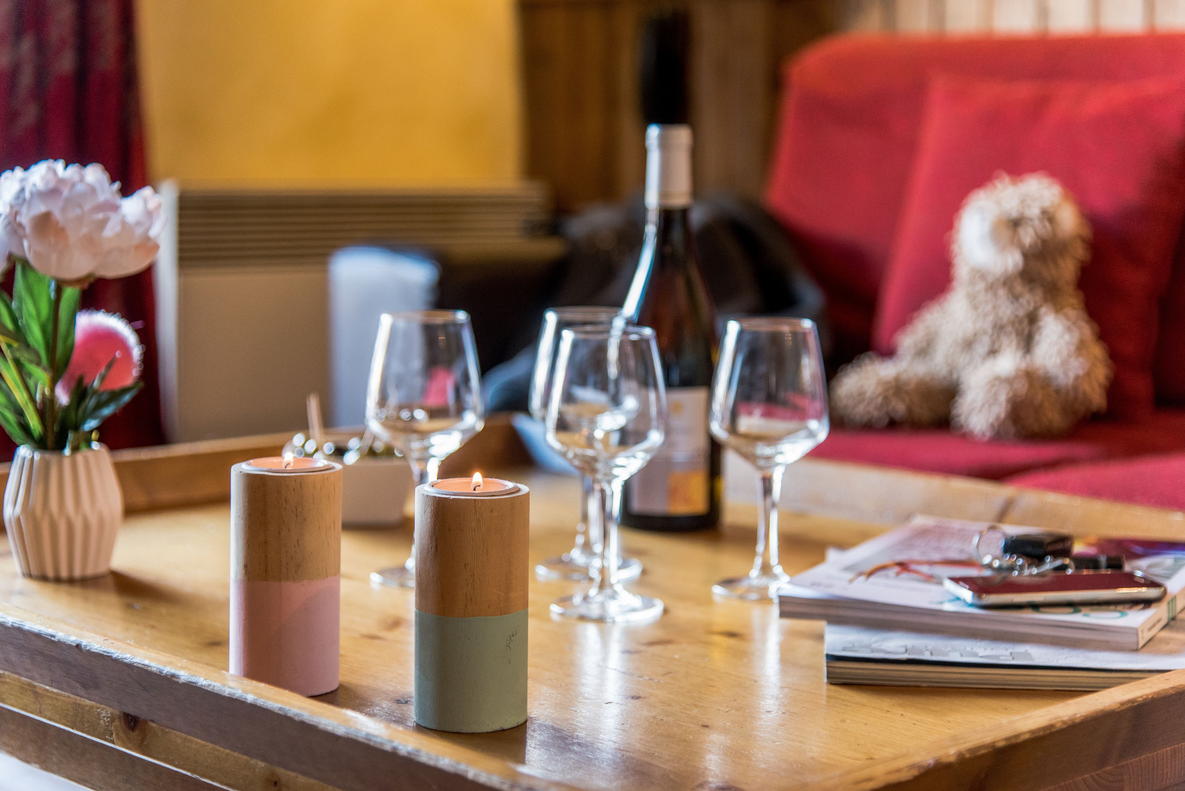 Une table en bois, décorée de bougies, de verres à vin, d’une bouteille et d’un ours en peluche.