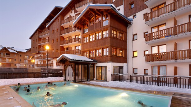 Un área de piscina con varios niveles de balcones de madera, una zona de estar cubierta y suelo cubierto de nieve.