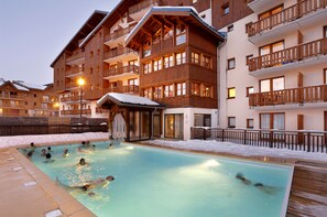 Un área de piscina con varios niveles de balcones de madera, una zona de estar cubierta y suelo cubierto de nieve.