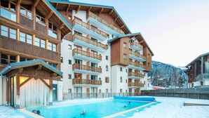 Un hotel de varios pisos con piscina, balcones de madera y una montaña nevada al fondo.