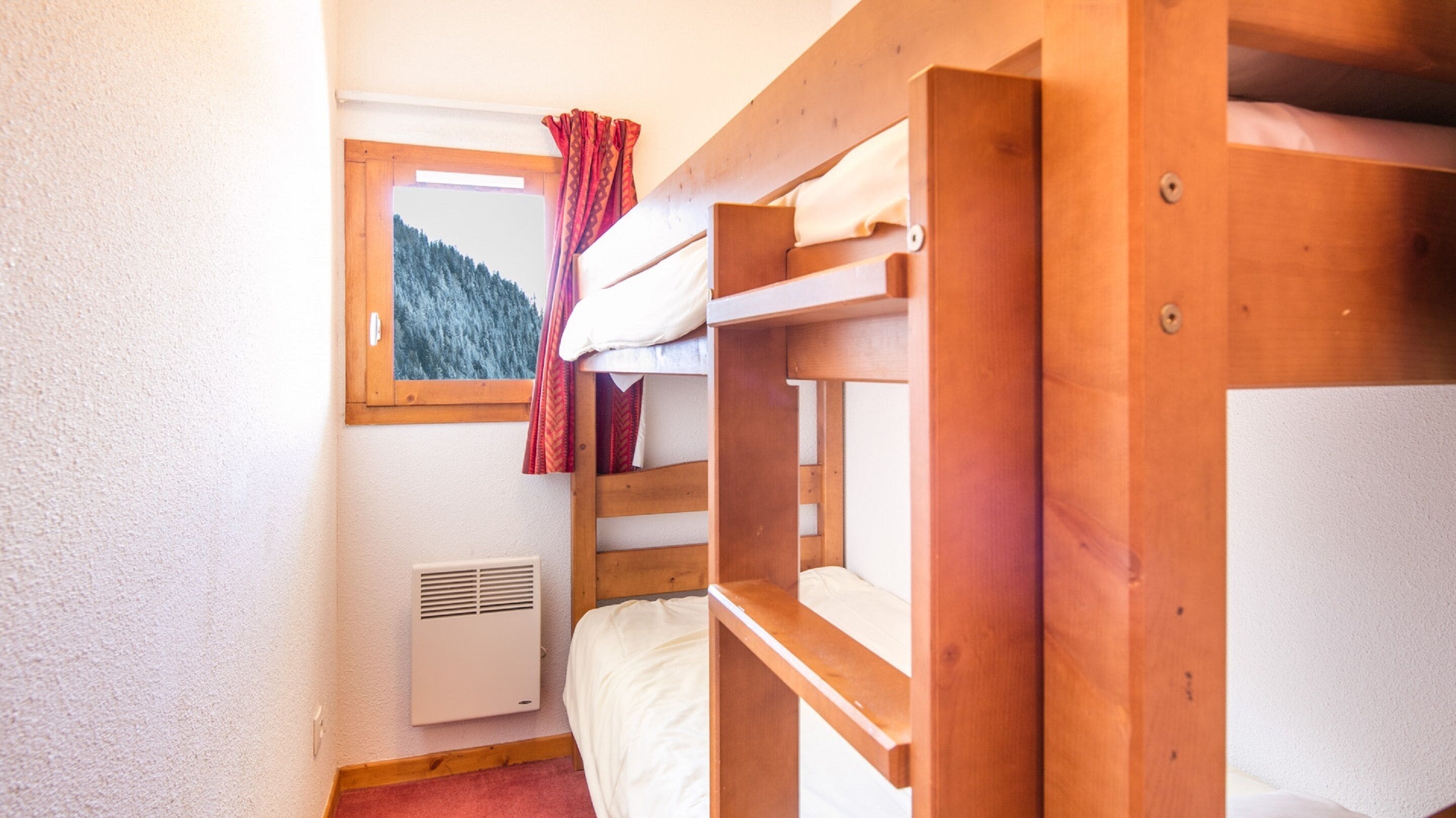A bunk bed room with a window, a radiator, and a view of a forested mountain.