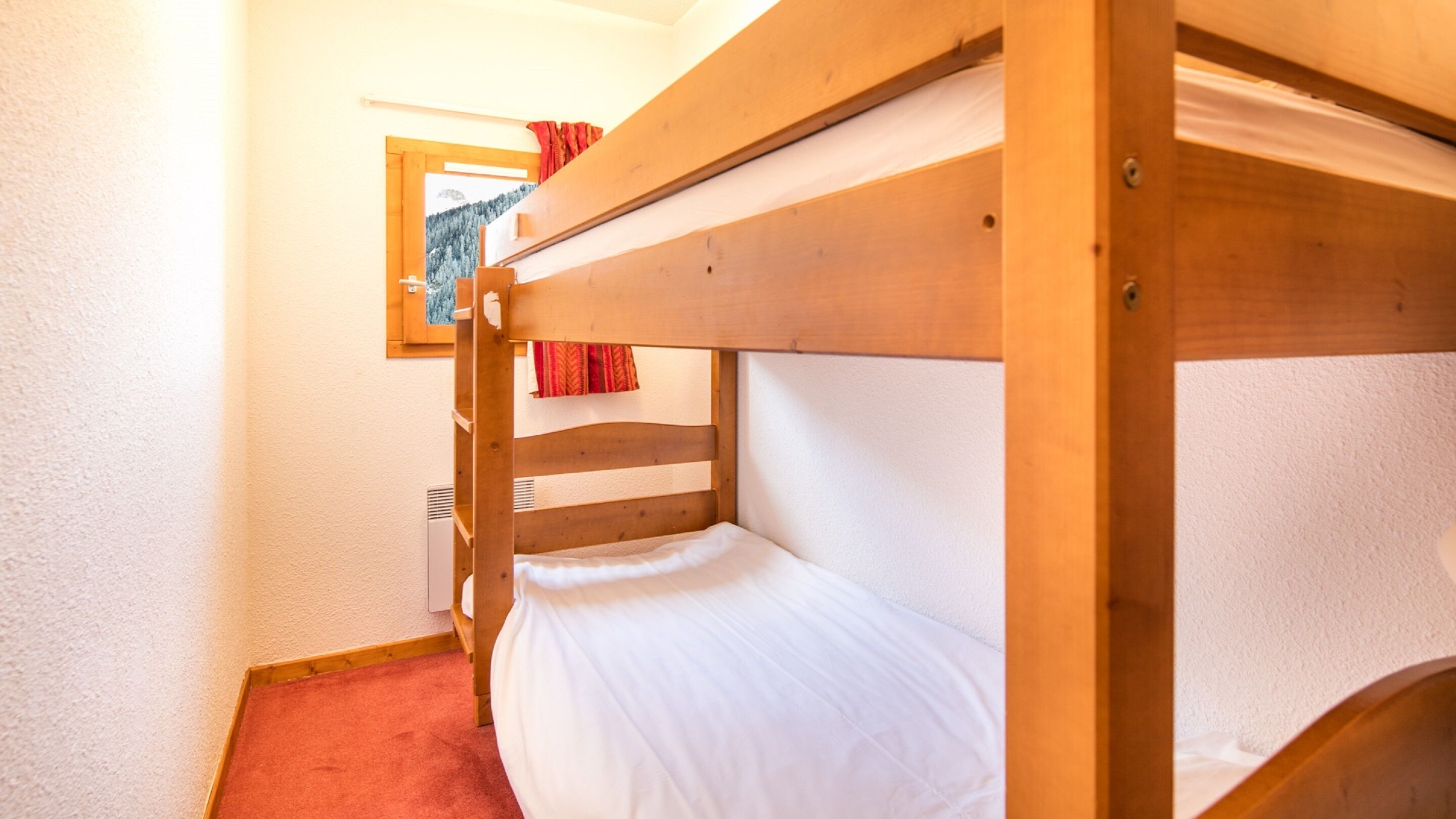 A bunk bed room with a wooden frame, white bedding, and a red carpet.