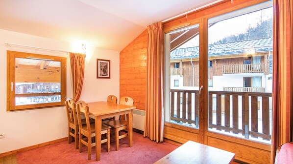 A wooden interior with a dining table, chairs, a radiator, a window with curtains, and a framed picture on the wall. - Les Chalets de la Ramoure (Modane)