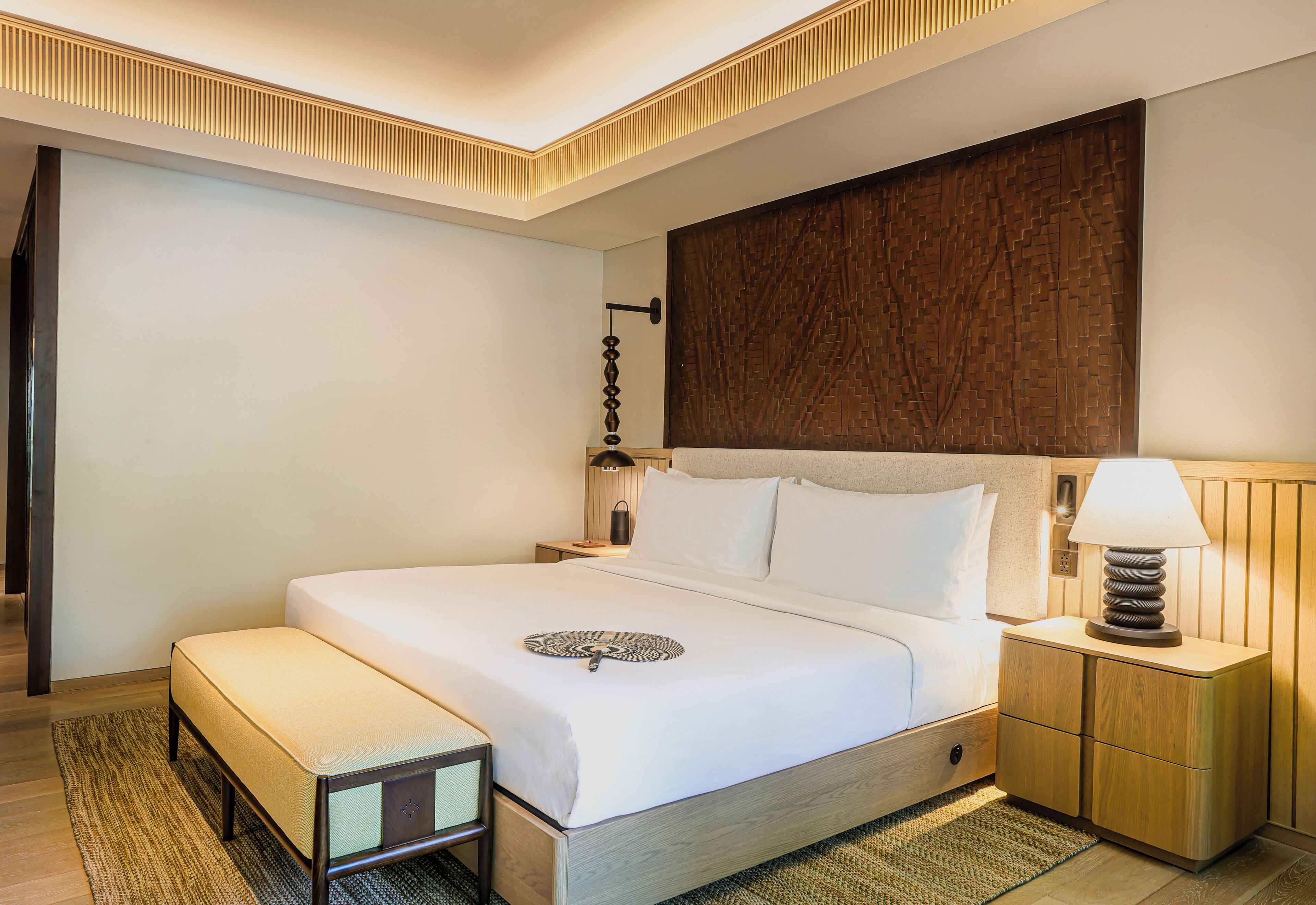 Una cama bien hecha con una mesita de noche, una lámpara de pared y un panel de pared texturizado.