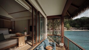 A balcony with a sofa, a small table, and a view of the sea. - Lagen Island Resort (El Nido)