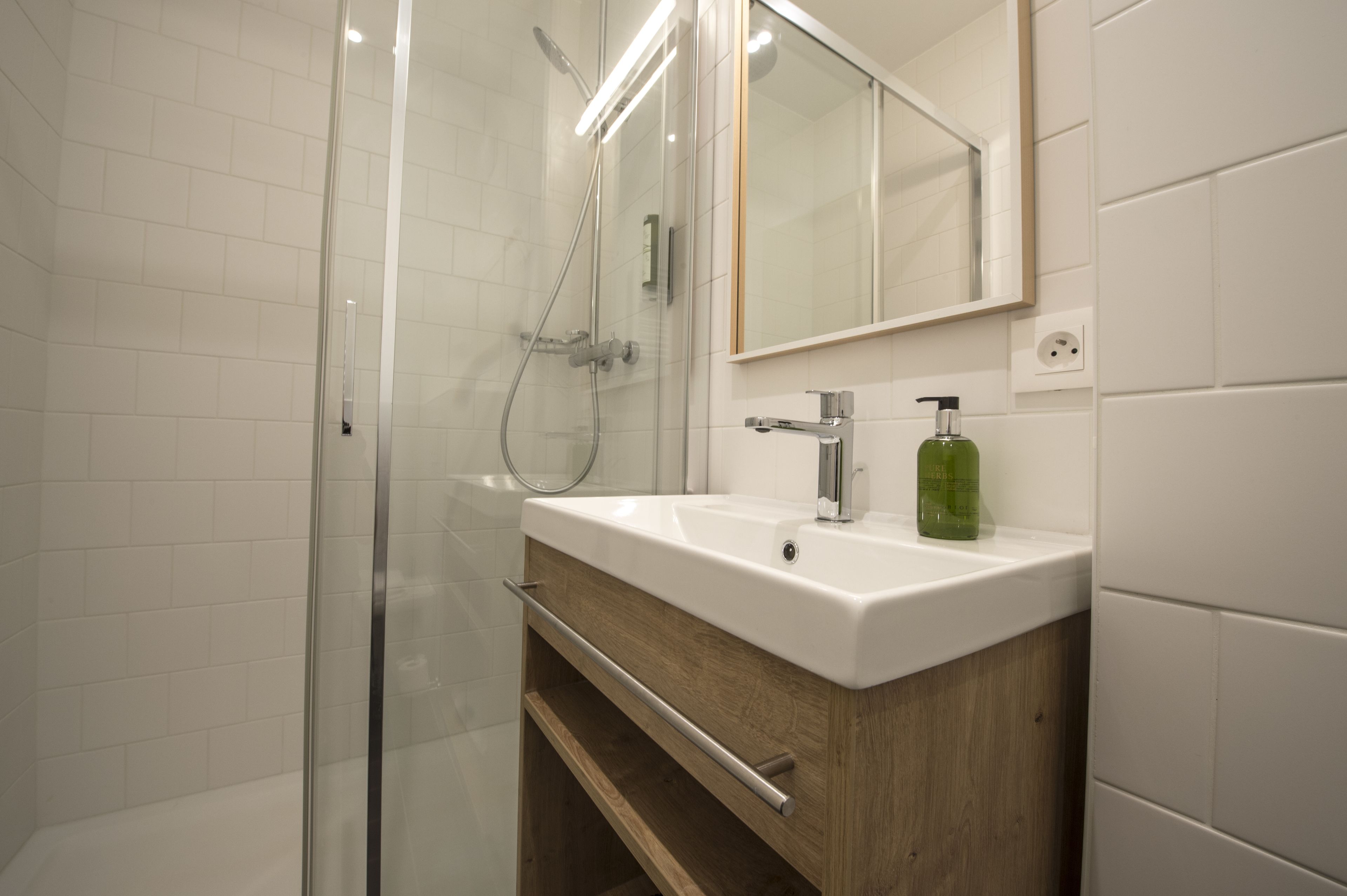 A modern bathroom with a glass shower enclosure, a white sink with a wooden vanity, and a mirror above the sink.