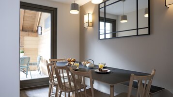 Un comedor con una mesa dispuesta para el desayuno, que incluye huevos, pasteles y jugo. Hay sillas de madera y un espejo grande en la pared.