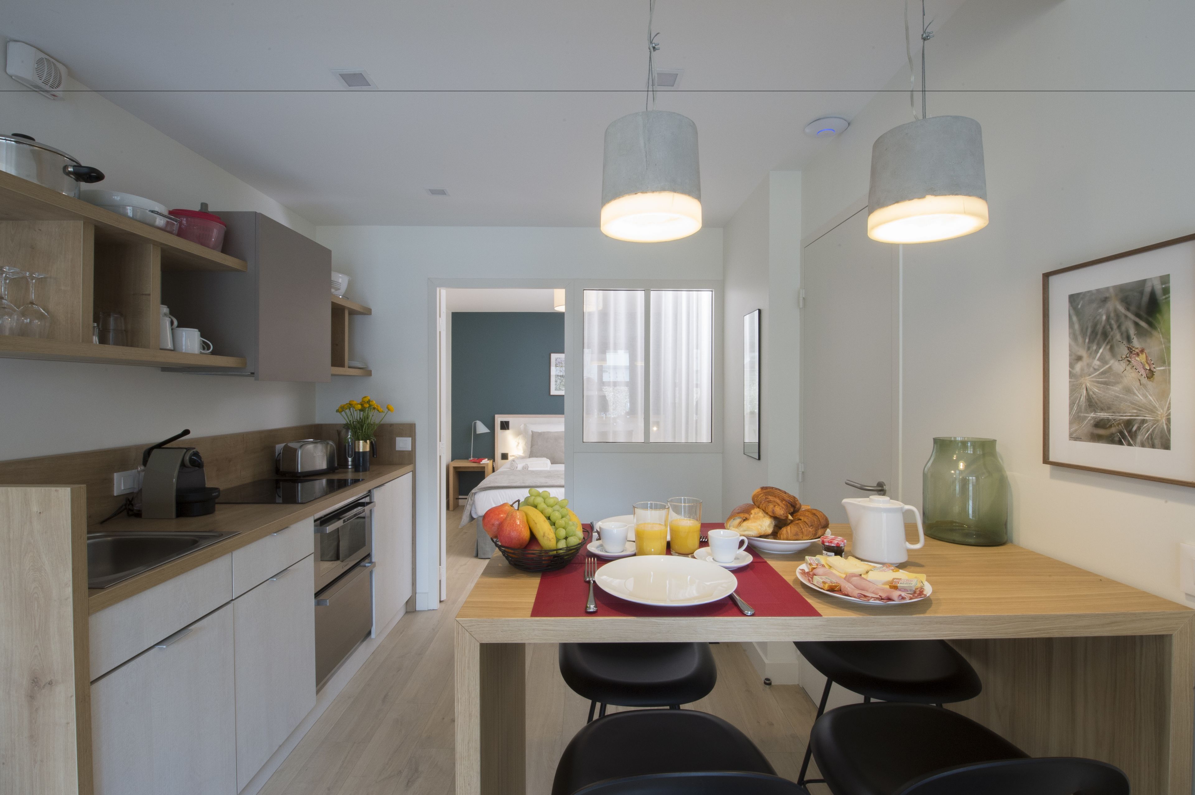 A modern kitchen with wooden countertops, a dining area with a breakfast setup including fruits, pastries, and a coffee pot.