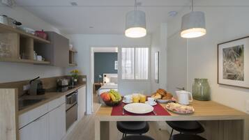 A modern kitchen with wooden countertops, a dining area with a breakfast setup including fruits, pastries, and a coffee pot.