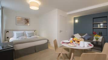 Una habitación de hotel moderna con cama, una mesa de comedor con desayuno, un sofá y una estantería.