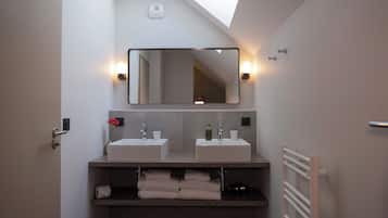 A modern bathroom with two sinks, a large mirror, and a skylight.