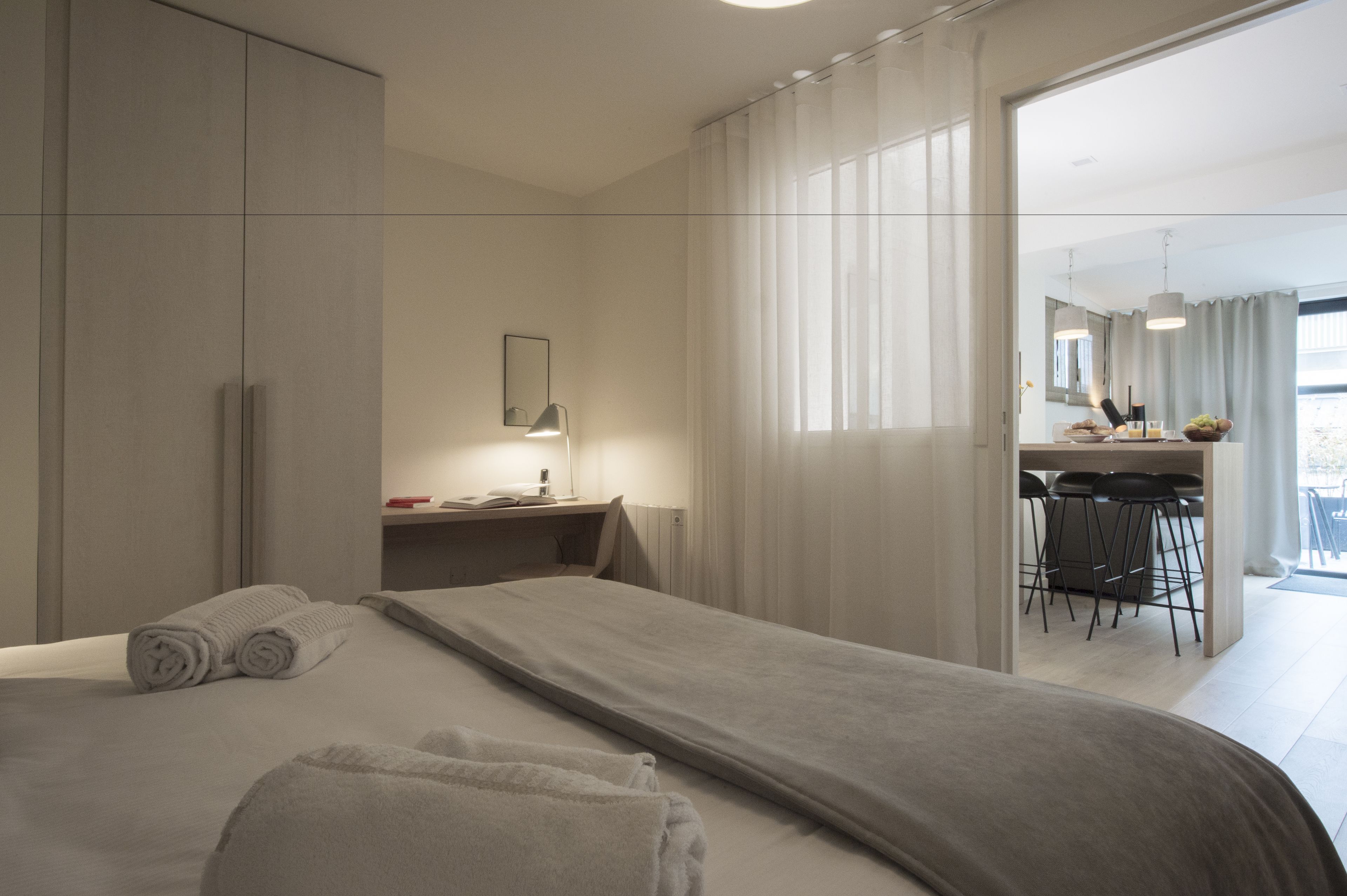 A modern hotel room with a large bed, a desk with a chair, and a view of the balcony.