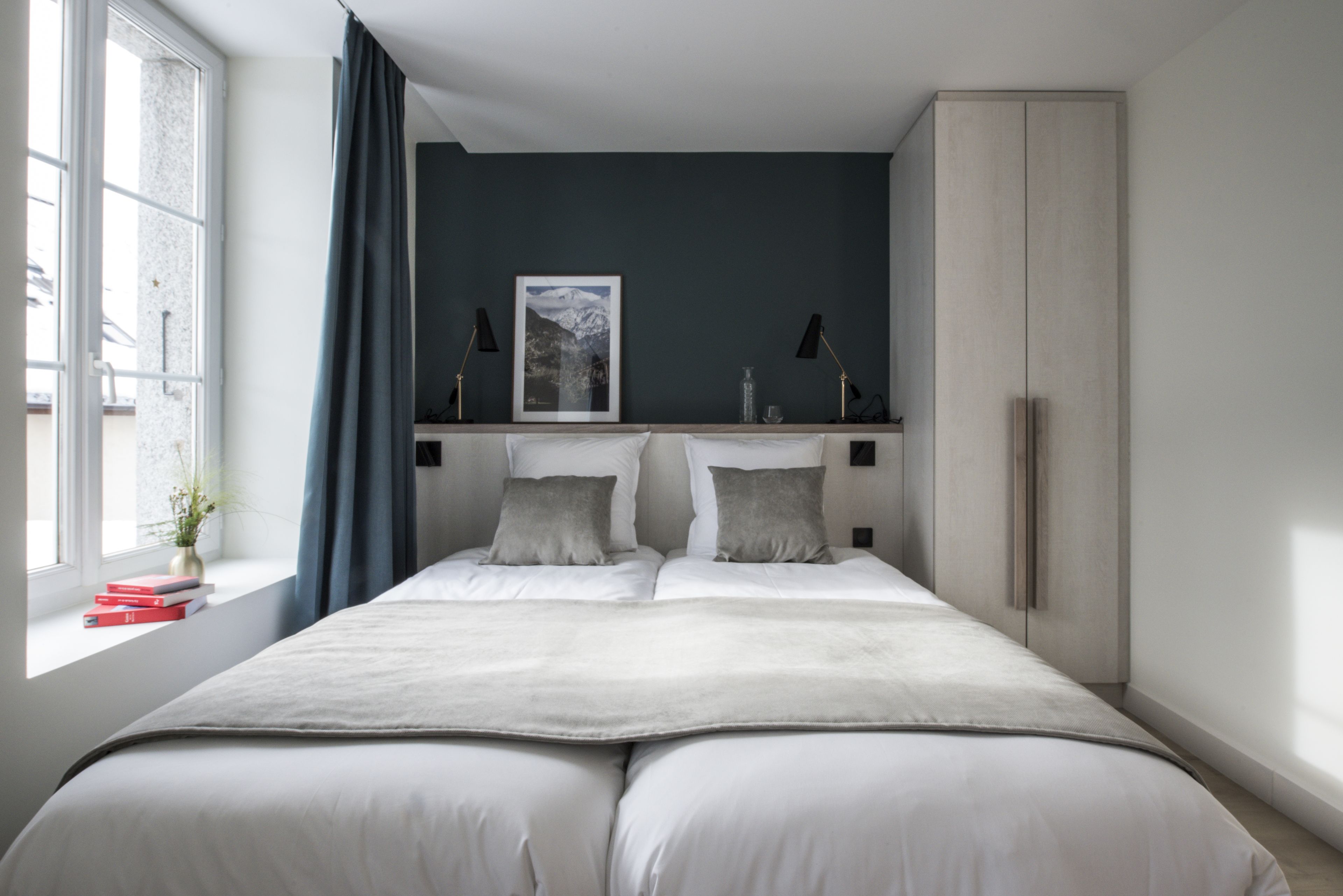 A bedroom with a large bed, a window with curtains, a bedside table with a lamp, and a framed picture on the wall.