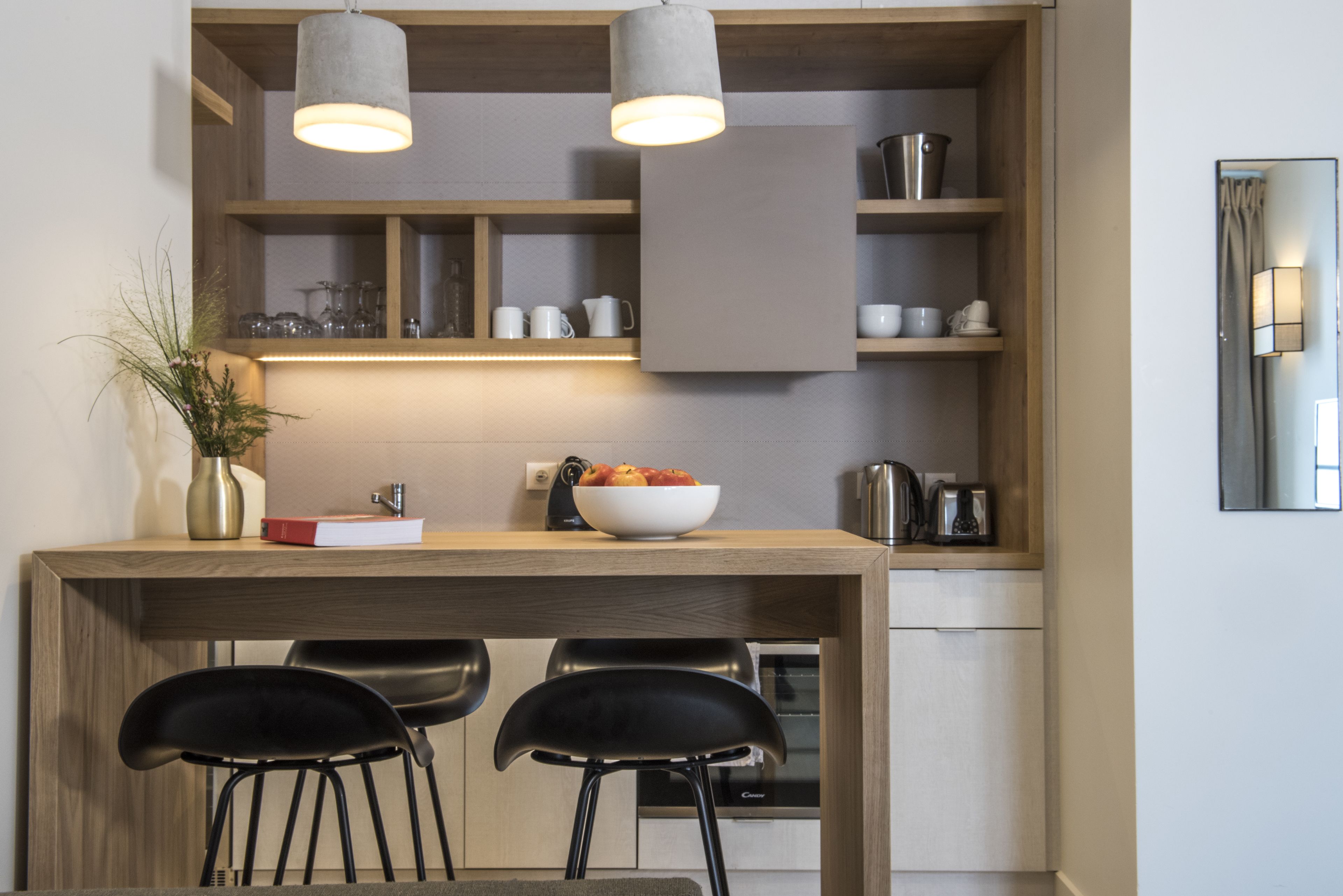A modern kitchen with wooden cabinetry, a central island with a bowl of fruit, two black chairs, and pendant lighting.