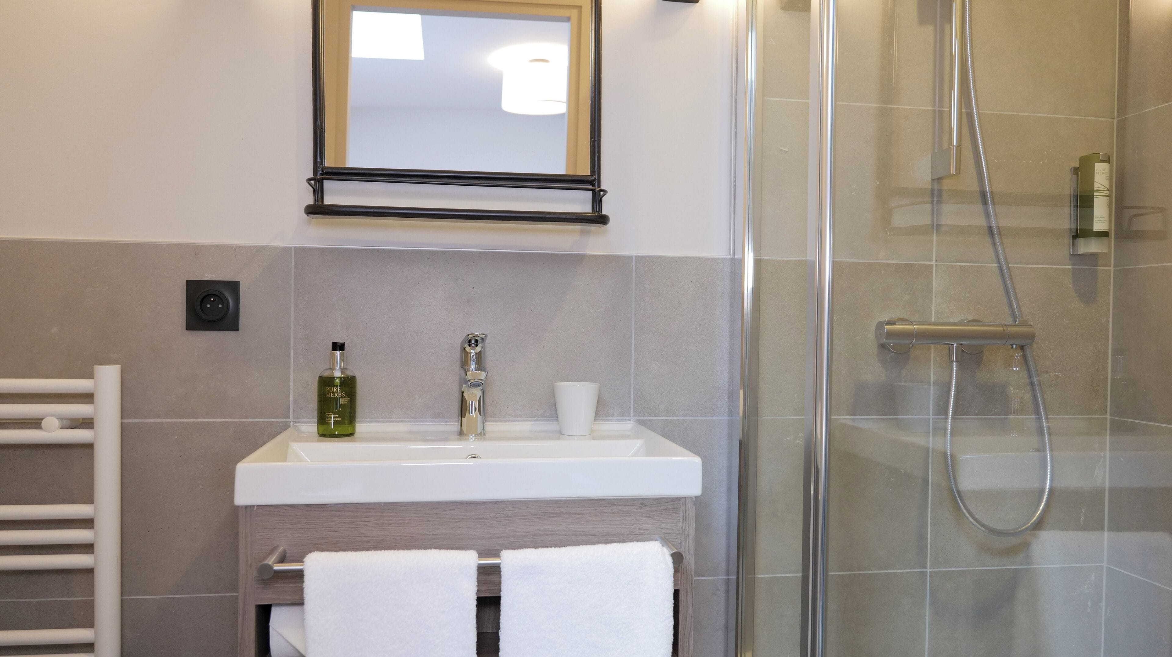 Un baño con ducha, lavamanos, espejo y toallero.