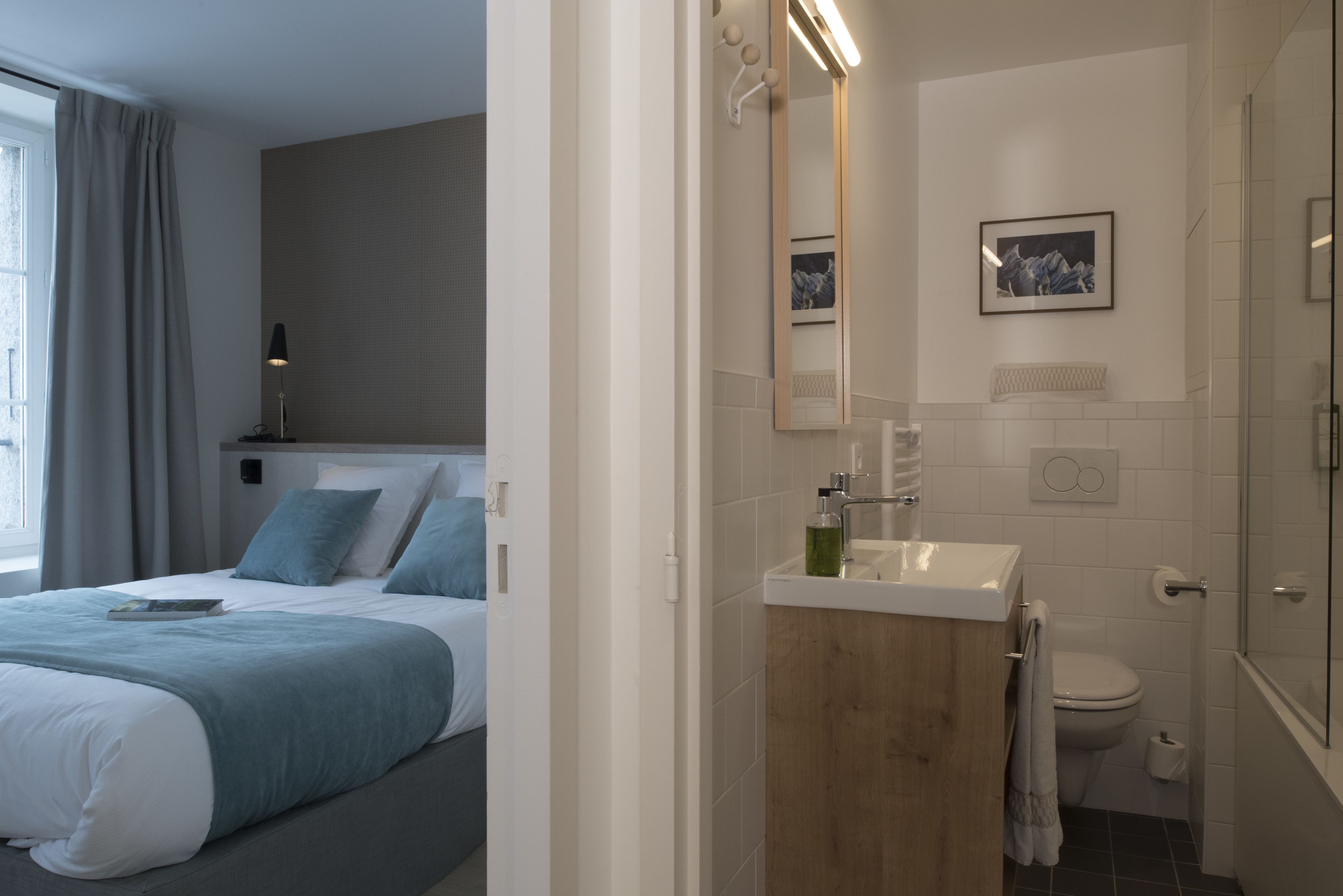 A modern hotel room with a neatly made bed, a bathroom with a sink, mirror, and toilet.