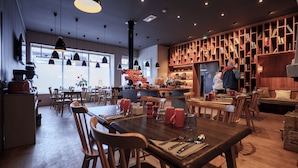 A restaurant interior with wooden furniture, pendant lighting, and a bookshelf filled with books and decorative items. - Appart'Hôtel le Génépy (Chamonix-Mont-Blanc)