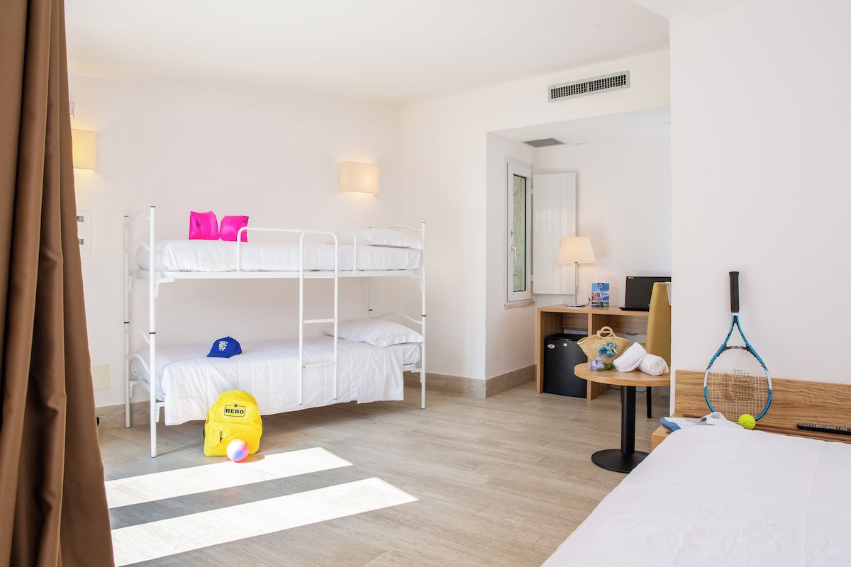 A hotel room with bunk beds, a desk with a lamp, a chair, a small table with a handbag, and a tennis racket.