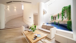 A modern interior with a spiral staircase, a pool area with greenery, and a seating area with a table and plant. - TH Simeri - Simeri Village (Simeri-Crichi)