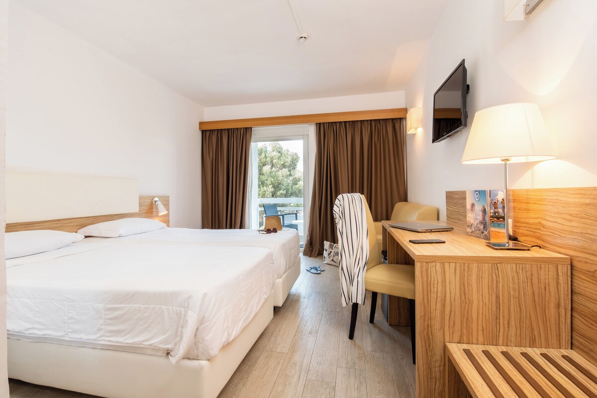 A hotel room with a bed, desk, chair, lamp, and a television on the wall.