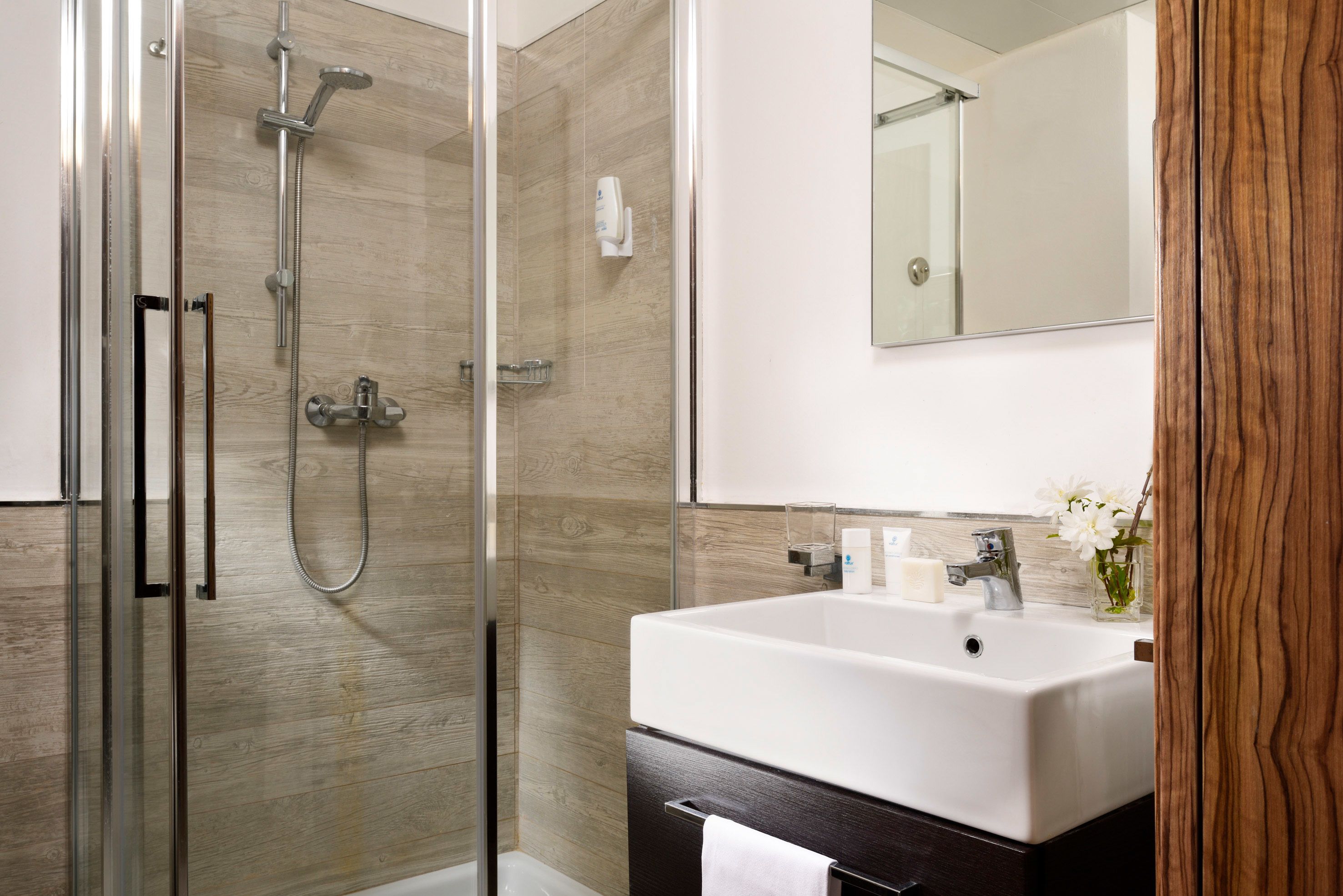A modern bathroom with a glass-enclosed shower, a white sink, and a mirror above it.