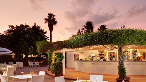 An outdoor dining area with tables and chairs, a bar with a counter, and a palm tree. - TH Simeri - Simeri Village (Simeri-Crichi)