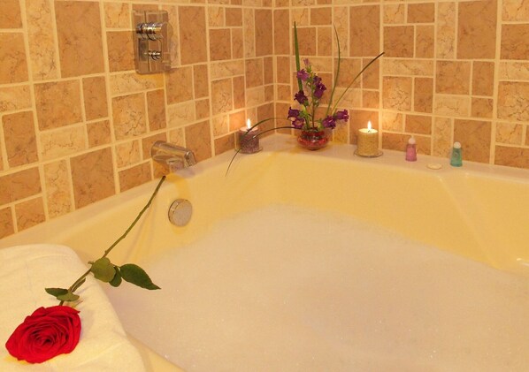 A bathtub with a rose, candles, and a vase of flowers.