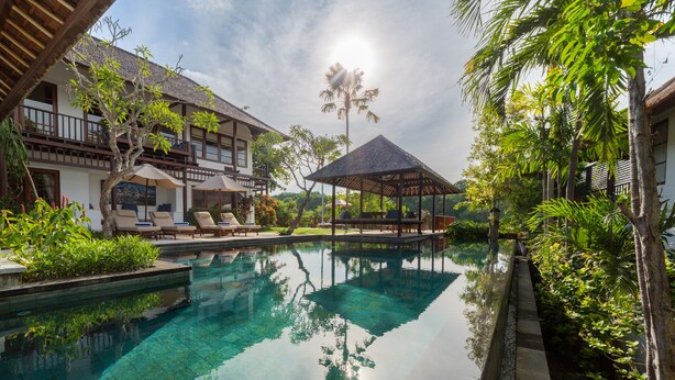 A clear pool with lounge chairs, a gazebo, and lush greenery.