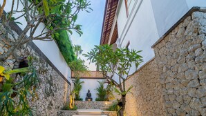 A stone staircase leading to a meditation area with a statue, surrounded by greenery and a white building.