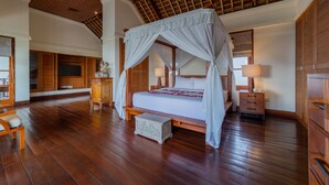 A spacious bedroom with a wooden floor, a canopy bed, wooden cabinets, and a large wardrobe.