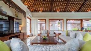 A spacious living room with a wooden ceiling, a large television, and a sofa with patterned cushions.