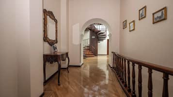Un passadís amb sòl de fusta, una banca de fusta, un mirall i una escala amb barana de fusta.