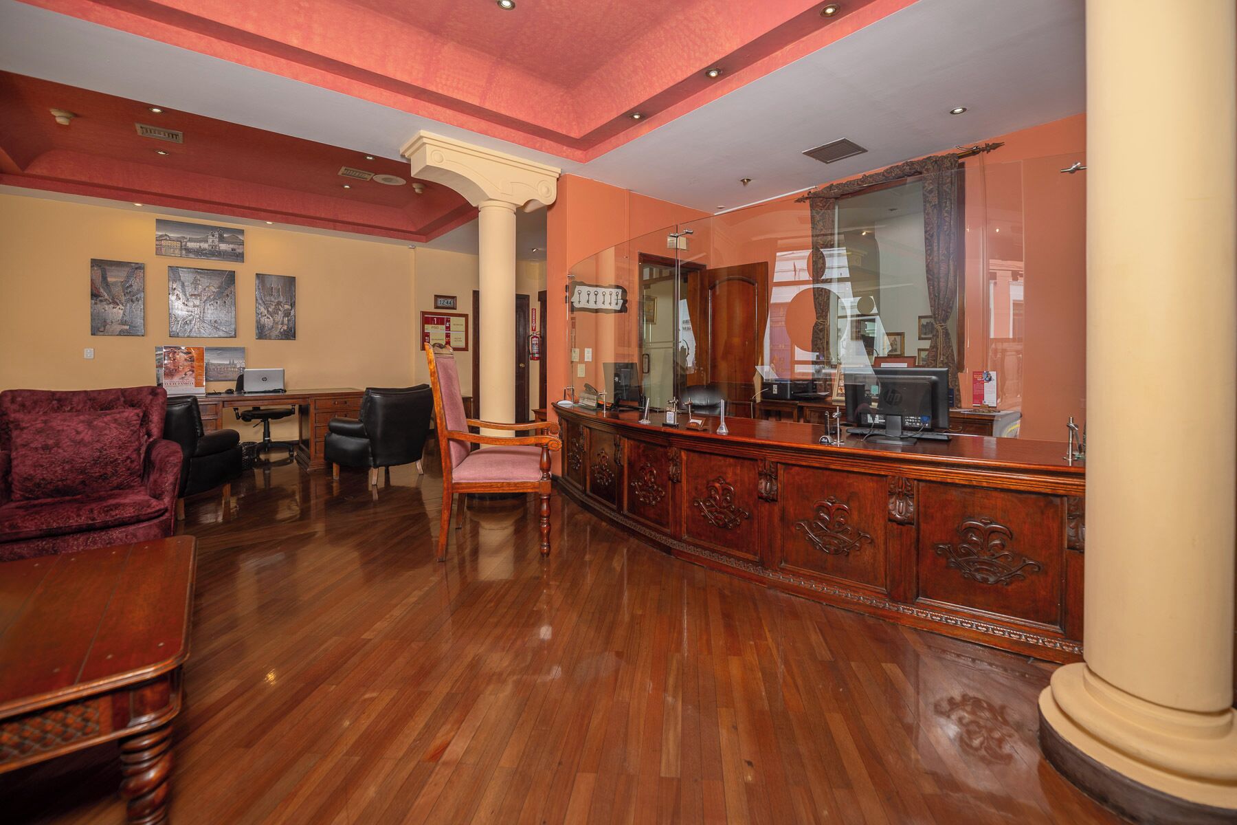 A lobby with a wooden reception desk, a red velvet sofa, and a large mirror.