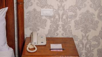 A wooden bedside table with a white telephone, a pen, and a piece of paper.