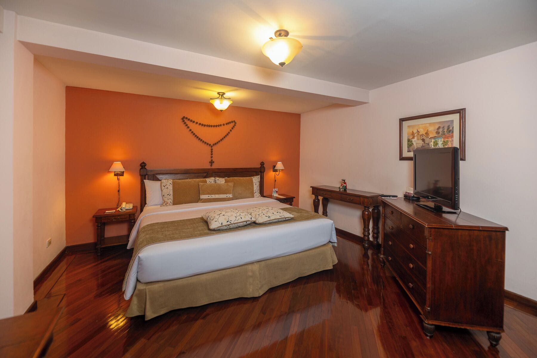 Un dormitorio con una cama de madera, dos mesitas de noche con lámparas, un aparador y un televisor en la pared.