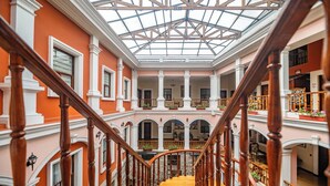 A grand staircase with a glass ceiling leading to multiple balconies, surrounded by ornate columns and a warm orange wall. - Hotel Patio Andaluz (Quito)